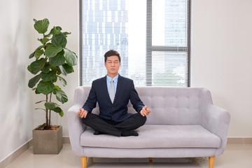 A young businessman meditating on sofa in office