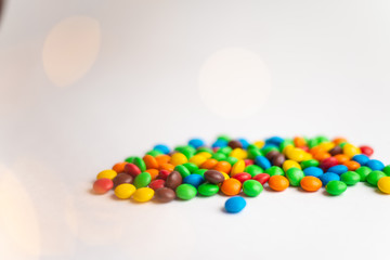 Obraz premium Coated chocolate multicolor candies on the white background with bokeh lights