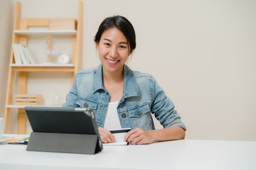 Beautiful smart business Asian woman using tablet buying online shopping by credit card while wear smart casual sitting on desk in living room at home. Lifestyle woman working at home concept.