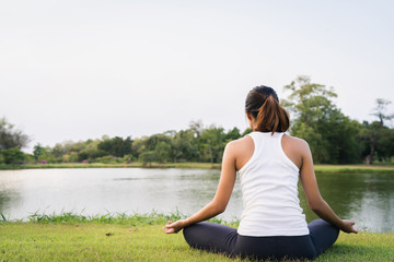 Fototapeta na wymiar Young asian woman yoga outdoors keep calm and meditates while practicing yoga to explore the inner peace. Yoga have good benefits for health near lake at park. Sport and Healthy lifestyle concept.
