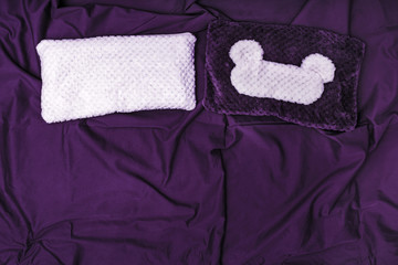 Soft pillow and sleep mask on dark violet crumpled sheet.  Top  view. Flat lay.