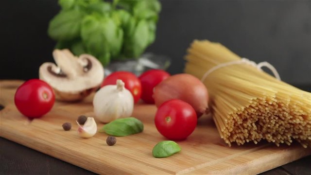pasta ingredients on wooden table panning shot .spaghetti cherry tomatoes mushrooms onion basil garlic