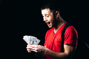 a man in a red t-shirt on a black background with a pack of money emotionally reacts