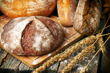 Freshly baked bread of different types and shapes and wheat ears on the wooden boards