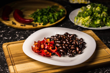 Black beans with sweet peppers on a white plate and wooden board.