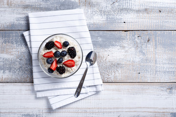 oatmeal with berries and spoon on light rustic wooden background