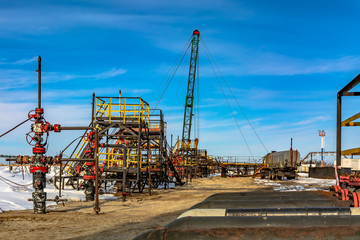 Fototapeta na wymiar Oil field in Siberia. In a row are oil producing wells. In the background, work is underway to overhaul the well. In the foreground is a manifold with valves.