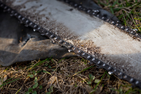 Close up of dirty chainsaw chain placed on ground on grass.
