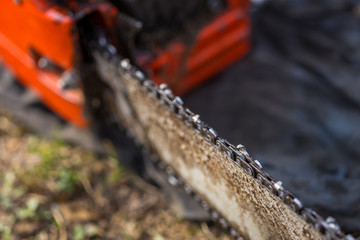 Close up of dirty chainsaw chain placed on ground on grass.