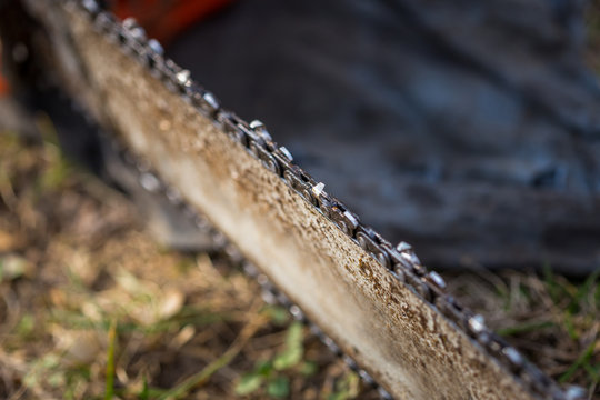 Close up of dirty chainsaw chain placed on ground on grass.