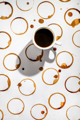 Cup of black coffee on a surface with many coffee stains.