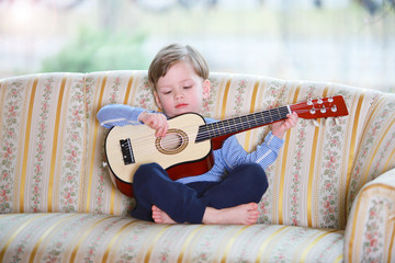 Ein dreijähriger Junge spielt auf einer Gitarre