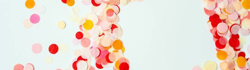 Colorful frame made with red and orange festive confetti on pastel background.Long wide banner with copy space.