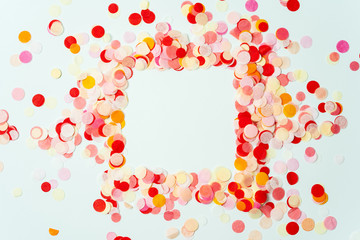 Colorful frame made with red and orange festive confetti on pastel background