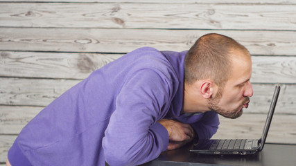 A short haired man kissing a computer screen.