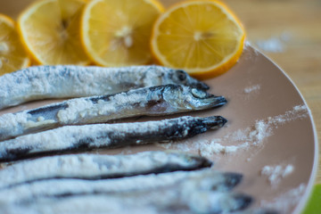 A fish rolled in flour lies on a beige plate.
