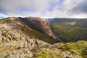 Two distant hikers sitting down on a rocky crag with distant views of Hopegill Head, Sand Hill and Grasmoor in the English Lake District, UK.