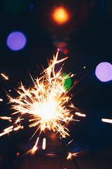 Fototapeta premium sparkling Bengal sparklers sticks in flames on a black background with lights bokeh. christmas theme new year background. holiday card