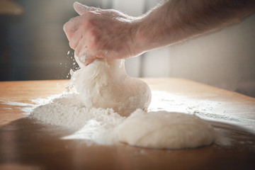 A man kneads dough on a wooden board in the afternoon.