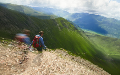 A female hiker and their dog descending from Grasmoor down Lad Hows above Buttermere on a sunny day...
