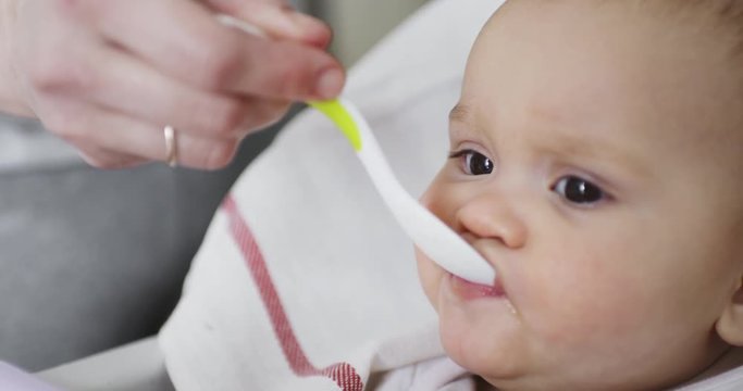 Closeup shot of mom feeds her little 8 months old baby from a spoon
