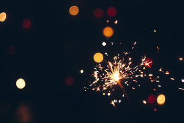 Obraz premium sparkling Bengal sparklers sticks in flames on a black background with lights bokeh. christmas theme new year background. holiday card
