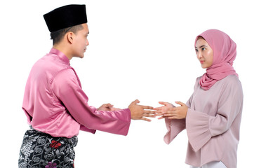 Portrait of young man with traditional clothing shaking hand his wife during hari raya over white background