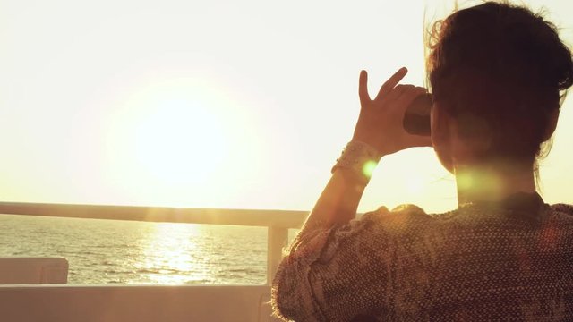Young woman enjoying sunrise on travel at sea. Taking pictures of the ocean on a ferry on cruise ship vacation