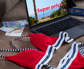 Bright swimsuit and money on the background of the open screen modern laptop with the description super price. Vacation planning. Early booking of tours.