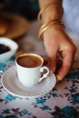Close up of hand serving cup of delicious strong Turkish coffee with creamy surface - khave- during Turkish breakfast in Istanbul cafe/ edited in warm colors. Travel and food in Turkey. 