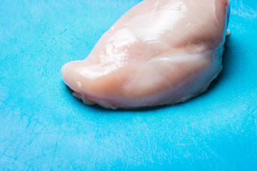 Fresh piece raw chicken on blue meat cutting board.