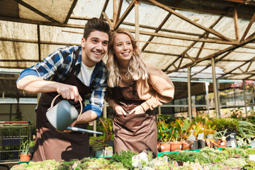 Happy young two colleagues gardeners at the workspace over plants