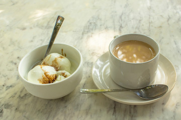 coffee with milk and ice cream balls in white cups with spoons on a marble table surface close up