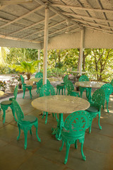 Fototapeta na wymiar empty restaurant under a white canopy among green palm trees with marble tables and green wrought-iron chairs