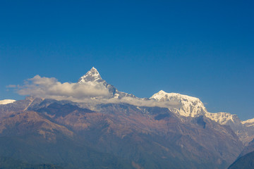 Obraz premium hillsides with green forests on the background of desert mountains and the snowy ridge of Annapurna with clouds under a clear blue sky. Machapuchare Himalayas Nepal