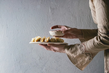 Fried asian dumplings Gyozas potstickers on white ceramic tray and bowl of soy sauce in female hands. Grey wall at background. Asian dinner