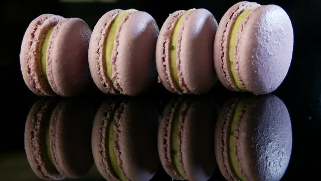 closeup human hand puts on edge five violet french dessert macaroon with green creamy filling in row on black background