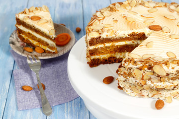 Close-up the  of vegetarian carrot cake  with almonds on white stand on blue wooden table.  The saucer with part of cake in the background.
