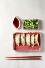 Fried asian dumplings Gyozas potstickers in pink square ceramic plate served with chopsticks, bowl of soy sauce, chopped spring onion over white marble background. Flat lay, space. Asian dinner