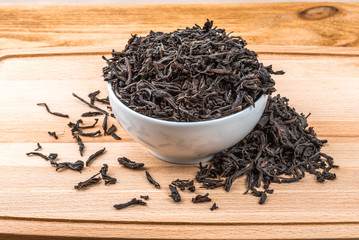 Dried tea is poured into a ceramic cup on a wooden plank table.