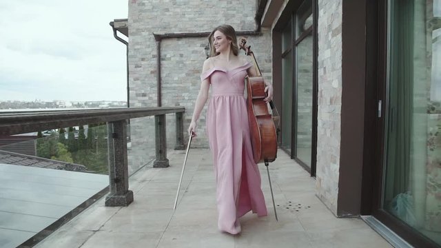 Smiling cellist walks on the balcony and plays on the cello