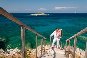 Romantic view of happy couple in white clothes cuddle and standing on rocky seashore. Picturesque...