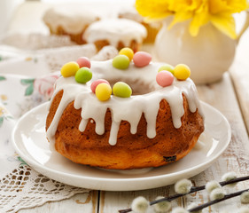 Easter yeast cake (Babka) covered with icing and decorated with marzipan eggs on a white plate on a wooden table. Traditional Easter cake in Poland