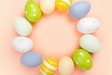 The circle of dyed on green, yellow and grey Easter eggs isolated on peach background. Easter theme flatlay.
