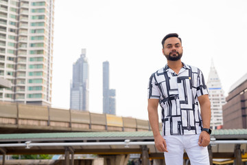 Young bearded Indian man against view of sky train station
