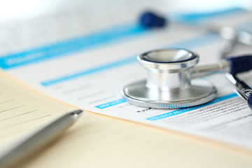 Stethoscope head and silver pen lying on medical application form