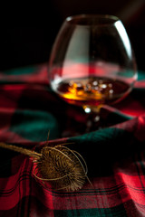 Glass of scottish whisly on a table with traditional tartan and a thisly, symbol of scotland