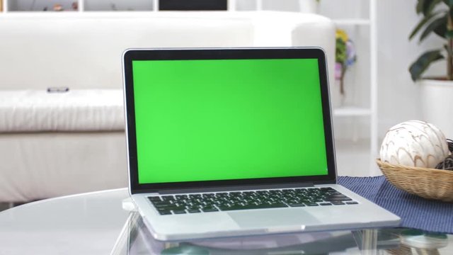 Laptop Computer Showing Green Chroma Key Screen Stands on a Desk in the Living Room. In the Background Cozy Living Room. Dolly Shot Left to right. 4K