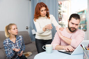 Upset young man working at laptop, young sister and mother
