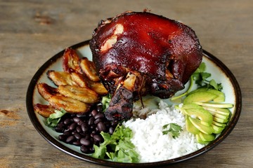 buddha bowl in latin american style. Colombian traditional food. pork knuckle ham baked, rice, black beans, fried bananas, avocado, cilantro. copy space. top view.